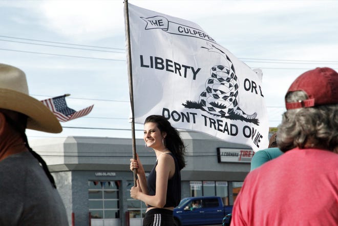 Ruth Culpepper holds a flag, Thursday, May 14, 2020, while protesting business restrictions in New Mexico that were enacted to reduce the spread of COVID-19.