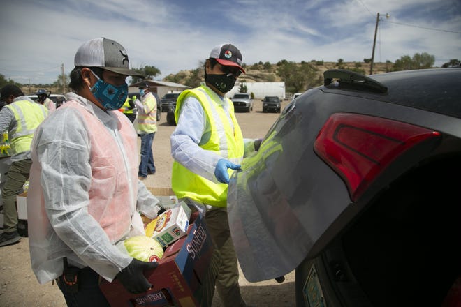 Navajo Nation President Jonathan Nez (center) and Isaiah Tsosie, an office specialist with the Coyote Canyon chapter, place food into a community member's vehicle at a food distribution point before the start of a weekend-long curfew in Coyote Canyon, New Mexico, in the Navajo Nation on May 15, 2020.