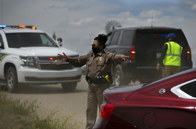Officer Netty Etsitty of the Navajo Tribal Police, directs traffic for people to receive food in their vehicles at a food distribution point before the start of a weekend long curfew, in Coyote Canyon, N.M., on the Navajo Nation on May 15, 2020. All businesses including the 13 grocery stores on the reservation were closed during the weekend long curfew to combat the new coronavirus pandemic. The Navajo Nation has been one of the hardest hit areas from the COVID-19 pandemic in the entire United States.