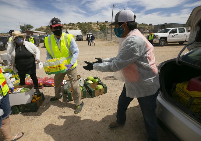 Navajo Nation President Jonathan Nez (center) and Isaiah Tsosie (right), an office specialist with the Coyote Canyon chapter, place bottled water into a community member's vehicle at a food distribution point before the start of a weekend-long curfew in Coyote Canyon, New Mexico, on the Navajo Nation on May 15, 2020.