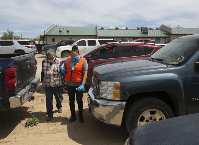 Candice Spencer (center), a volunteer, helps Christine Tso (left) back to her vehicle as Tso waits to receive food at a food distribution point before the start of a weekend-long curfew in Coyote Canyon, New Mexico, on the Navajo Nation, on May 15, 2020.