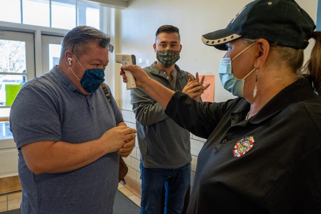 Dawn Kryder checks Chuck Griego's temperature while Elias Trujillo sanitizes his hands, before early voting at the San Miguel County Clerk's office in Las Vegas, New Mexico.